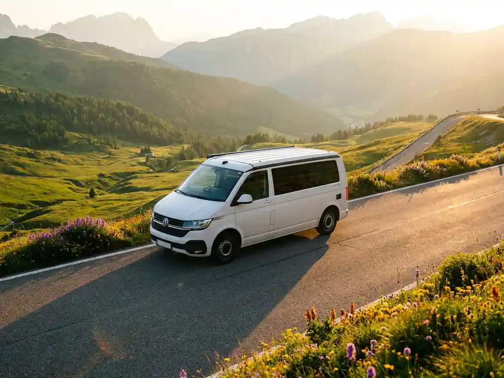 Witte moderne campervan op een schilderachtige Europese bergweg, omgeven door groene vallei en goudkleurig middaglicht.